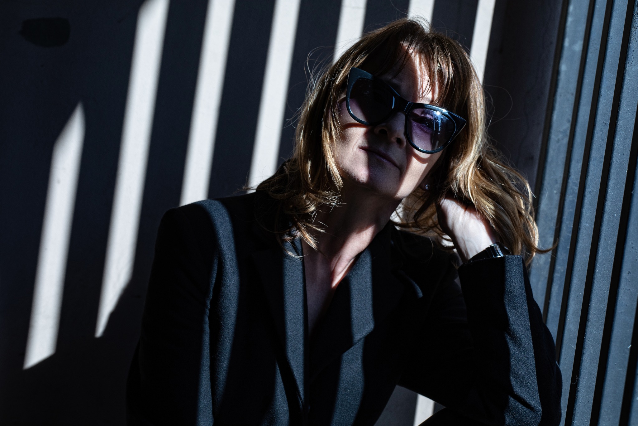 Portret kobiety w czarnym żakiecie i okularach przeciwsłonecznych, oświetlonej prążkami światła, wykonany w Zbrudzewie.