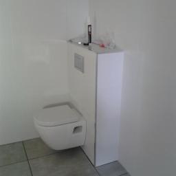 Glazurex - Wisząca toaleta z zabudowanym stelażem podtynkowym, białe płytki na ścianach, szare płytki podłogowe, widoczna tuba silikonu i folia na stelażu.