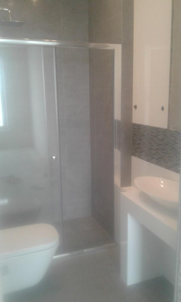 Nowoczesna łazienka z kabiną prysznicową ze szklanymi drzwiami przesuwnymi, umywalką nablatową na białej szafce i toaletą w minimalistycznym stylu.