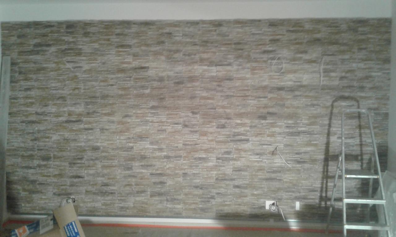 Ściana wykończona dekoracyjnym kamieniem w odcieniach szarości i beżu, widoczne wystające przewody elektryczne i drabina aluminiowa, sugerująca prace wykończeniowe w trakcie realizacji.