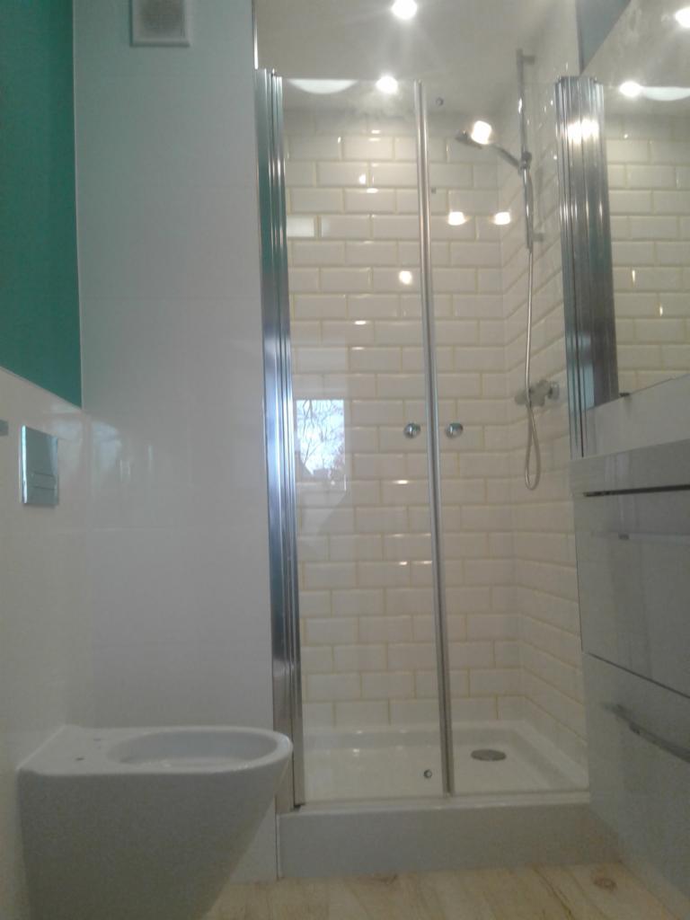 Nowoczesna łazienka z kabiną prysznicową z chromowanymi profilami, białą armaturą i białymi płytkami typu metro na ścianach.