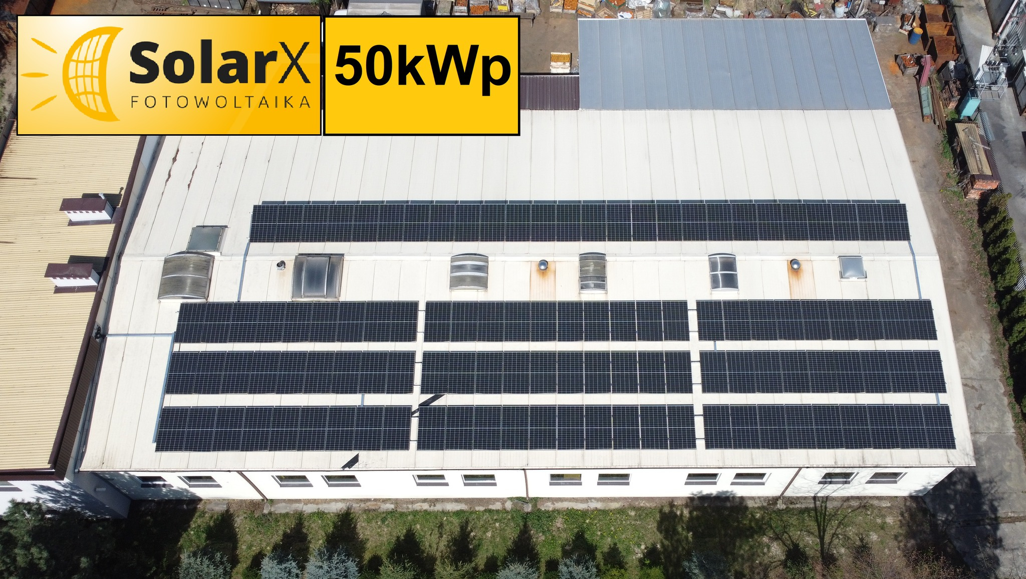 Widok z góry na dużą instalację paneli na dachu budynku przemysłowego, z logo firmy SolarX i oznaczeniem mocy 50kWp.