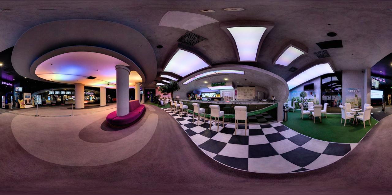 Panoramiczny widok wnętrza nowoczesnego lokalu z barem, stolikami i krzesłami, podświetlonymi elementami dekoracyjnymi i podłogą w szachownicę.