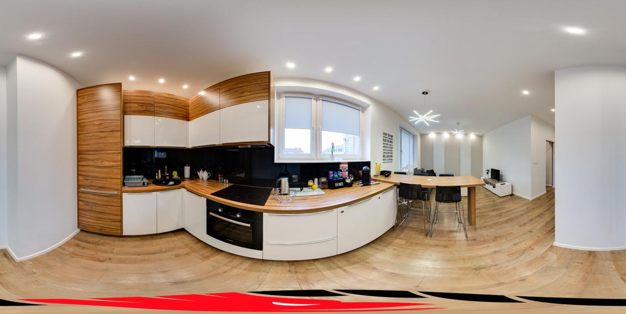 Wnętrze nowoczesnej kuchni z drewnianymi i białymi szafkami, blatem z drewna, czarnym panelem nad blatem, oknem z roletami, stołem z krzesłami barowymi i widokiem na salon