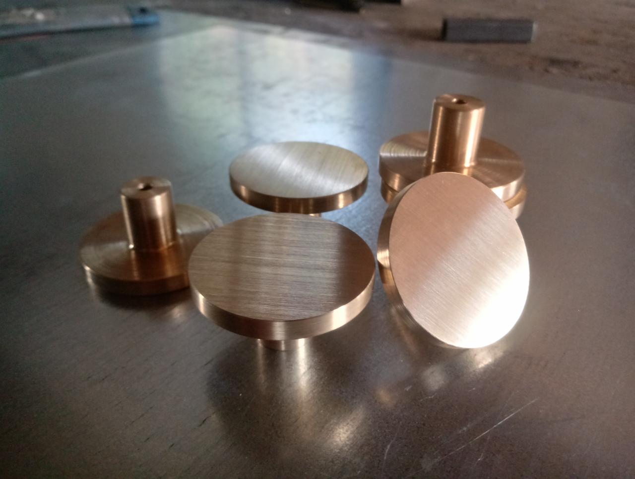 Pięć mosiężnych, okrągłych elementów obrobionych na tokarce, z widocznymi śladami obróbki, leżących na metalowej powierzchni.