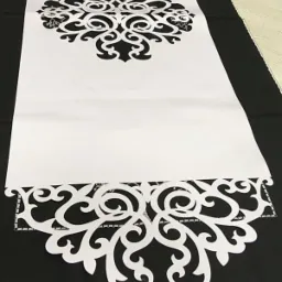 Biały bieżnik z ażurowym wzorem leżący na czarnym materiale, prezentujący precyzyjne wycięcia.