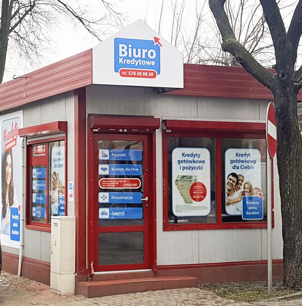 Fasada punktu kredytowego z szyldem 'Biuro Kredytowe' i ofertami pożyczek, kredytów gotówkowych, dla firm, konsolidacji i leasingu, widoczne plakaty reklamowe w oknach.