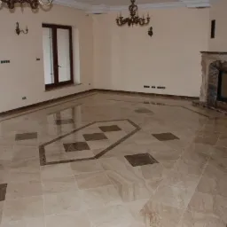 Elegancki salon w Warszawie z marmurową posadzką w geometryczny wzór i klasycznym kominkiem z kamienia.