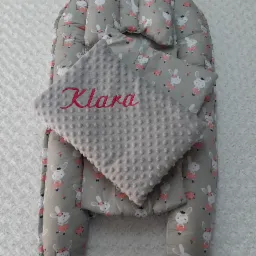 Dziecięcy kokon niemowlęcy z poduszką i kocykiem, szary materiał w króliczki baletnice, kocyk z wypukłą fakturą i czerwonym haftem imienia Klara.