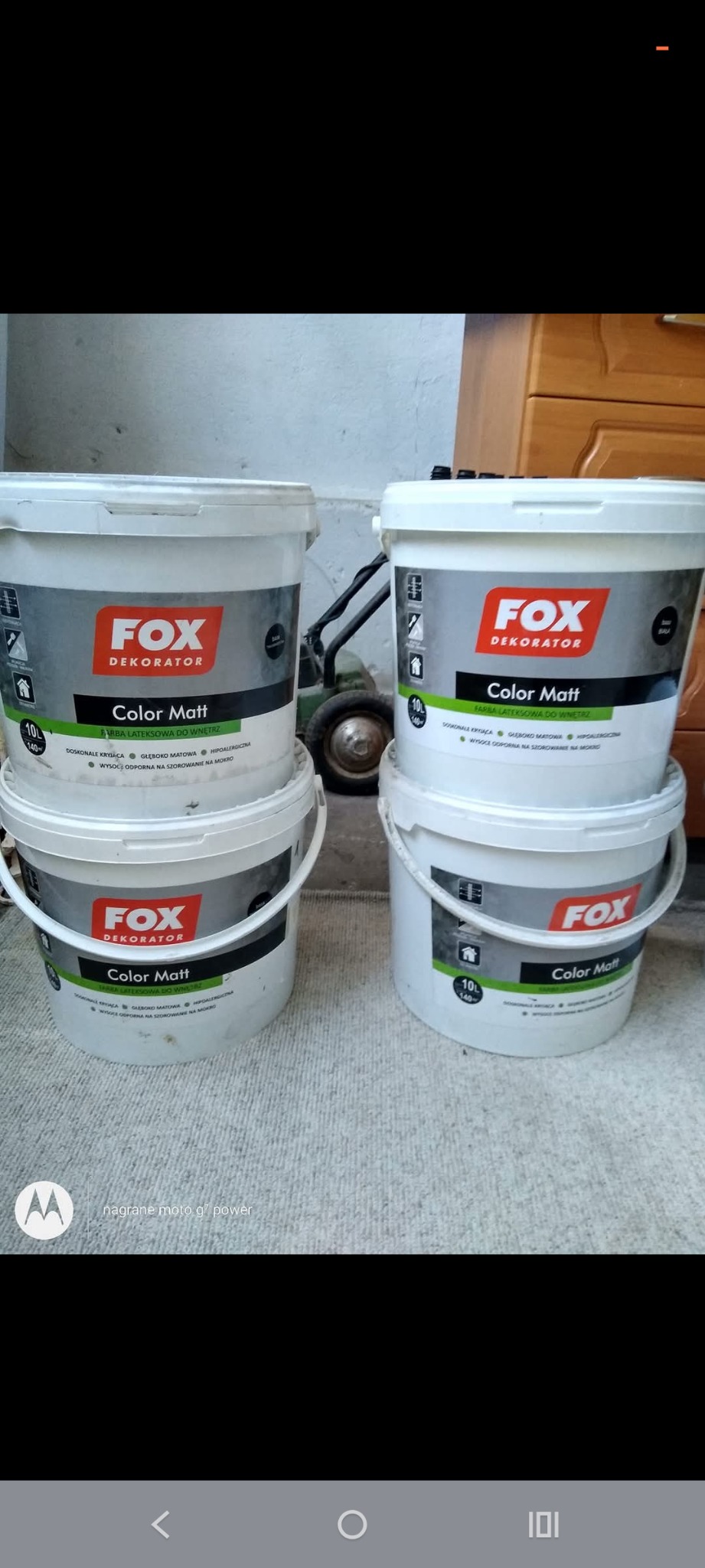 Stos czterech białych wiader z farbą lateksową Fox Dekorator Color Matt, ustawionych parami na podłodze. W tle widoczny fragment komody i wózek.