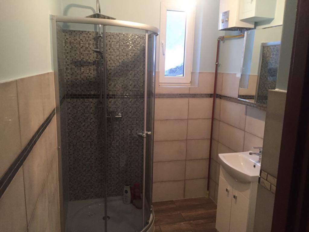 Ukończona łazienka z kabiną prysznicową z mozaiką, umywalką z szafką, grzejnikiem oraz oknem