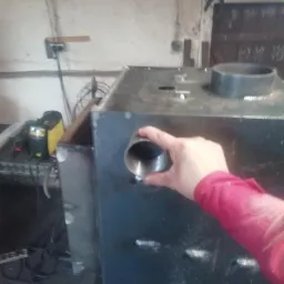 Metalowa konstrukcja w trakcie łączenia rur, widoczne spawy, w tle spawarka.