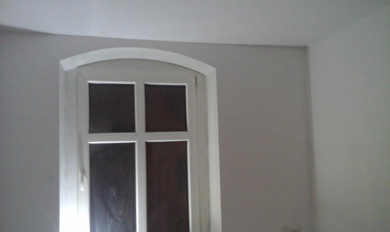 Wnętrze pokoju z odnowionym oknem o łukowatym kształcie ramy, pomalowanym na biało, na tle świeżo pomalowanej szarej ściany.