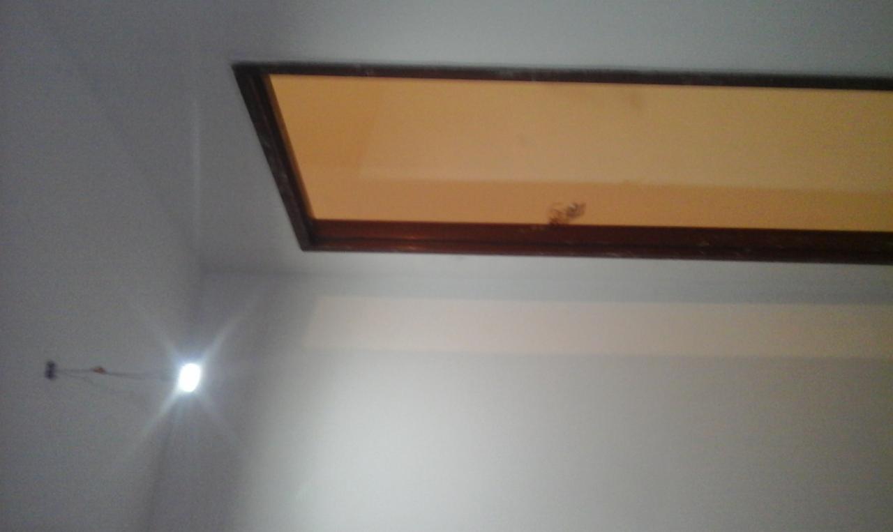 Fragment sufitu z osadzonym oknem dachowym w drewnianej ramie, widoczny kabel wystający ze ściany i plama na suficie.