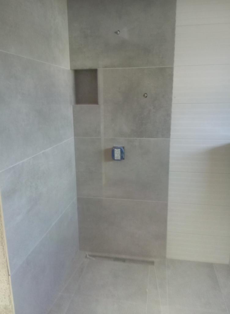 Wykończona łazienka z szarymi płytkami o matowej powierzchni, wnęka w ścianie, widoczne puszki elektryczne przygotowane do montażu osprzętu.