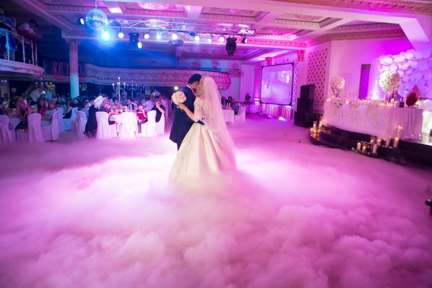 Para młoda tańczy pierwszy taniec w sali balowej wypełnionej sztuczną mgłą, oświetloną różowym światłem, z widocznymi gośćmi przy stołach w tle.