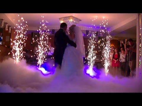 Para młoda tańczy w dymie i blasku fontann iskier podczas wesela, goście obserwują.