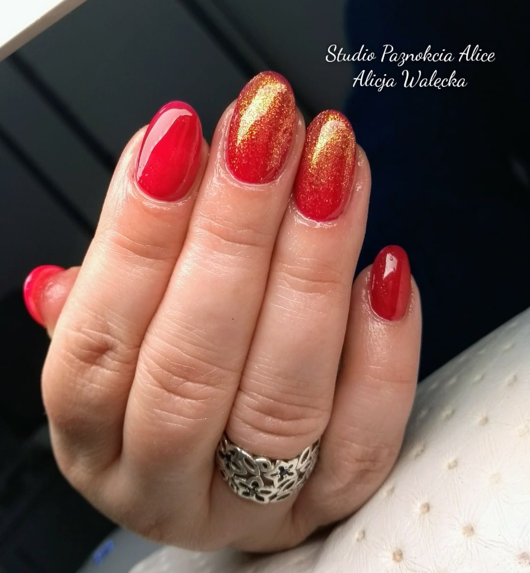 Dłoń z owalnymi paznokciami: dwa czerwone z połyskiem, dwa jednolicie czerwone, srebrny ażurowy pierścionek na palcu serdecznym.