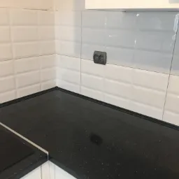 Wykończona kuchnia z czarnym blatem z brokatem, białe płytki z efektem 3D i szare gniazdko elektryczne