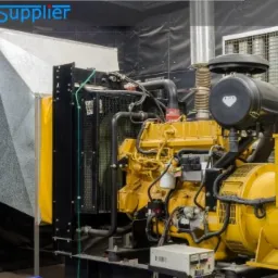 Żółty agregat prądotwórczy z metalową obudową i systemem wentylacji, widoczne przewody i tabliczka ostrzegawcza.