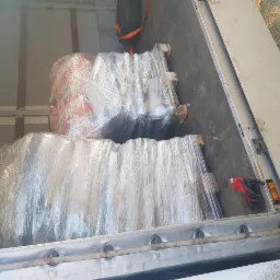 Wnętrze paki busa z załadowanym towarem na paletach, owiniętym folią stretch, widoczne rękawice robocze i zapasowe koło.