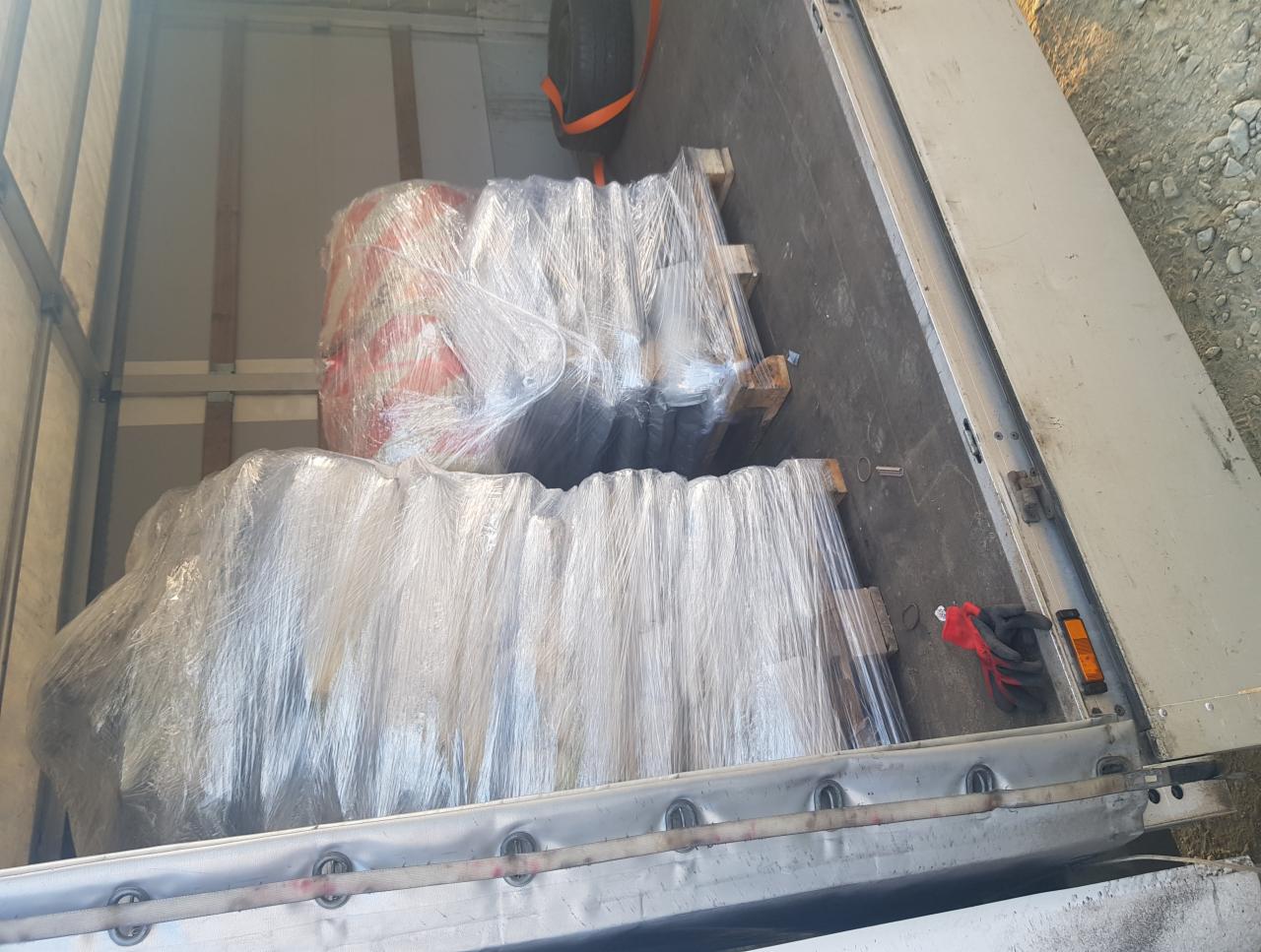 Wnętrze paki busa z załadowanym towarem na paletach, owiniętym folią stretch, widoczne rękawice robocze i zapasowe koło.