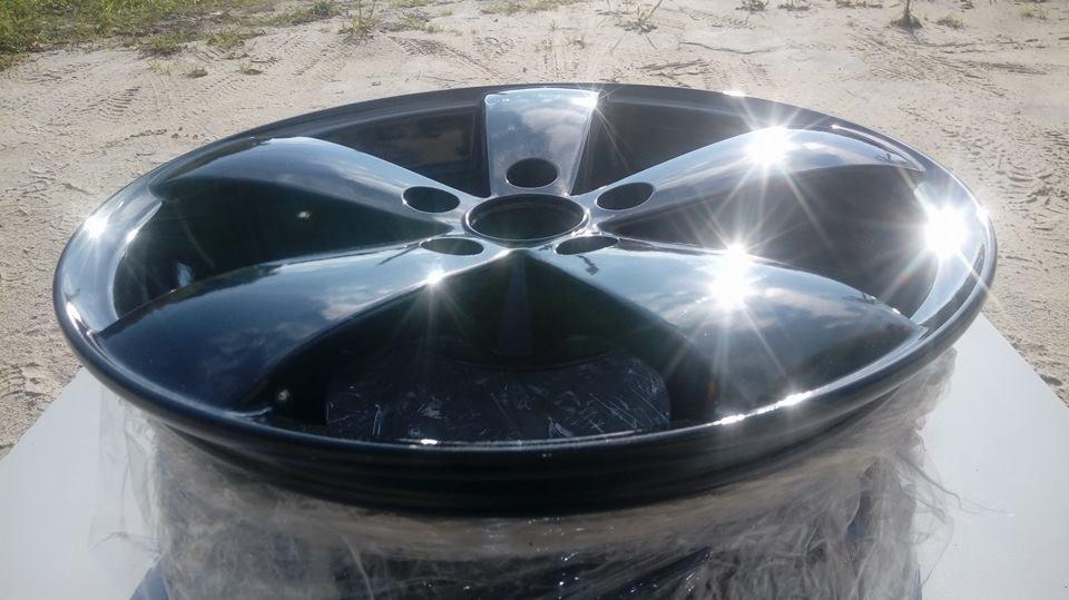 Błyszcząca, czarna felga aluminiowa z pięcioma ramionami, leżąca na folii ochronnej, z odbiciami słońca na powierzchni.