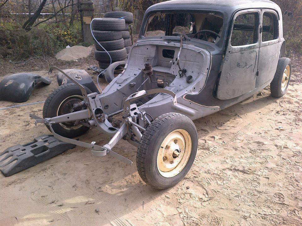 Demontaż starego samochodu do renowacji: szkielet karoserii z widocznymi elementami zawieszenia, opony ułożone w stos na zewnątrz, przygotowanie do prac blacharskich i lakierniczych.