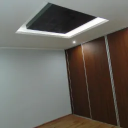 Pokój z drewnianą podłogą i szafą przesuwną, sufit z podwieszanym elementem z oświetleniem LED i ciemną wnęką.