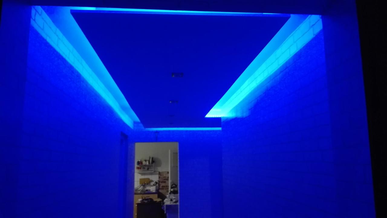 Korytarz z oświetleniem LED w kolorze niebieskim, podwieszany sufit z dekoracyjnym oświetleniem, widok na otwartą kuchnię w tle.