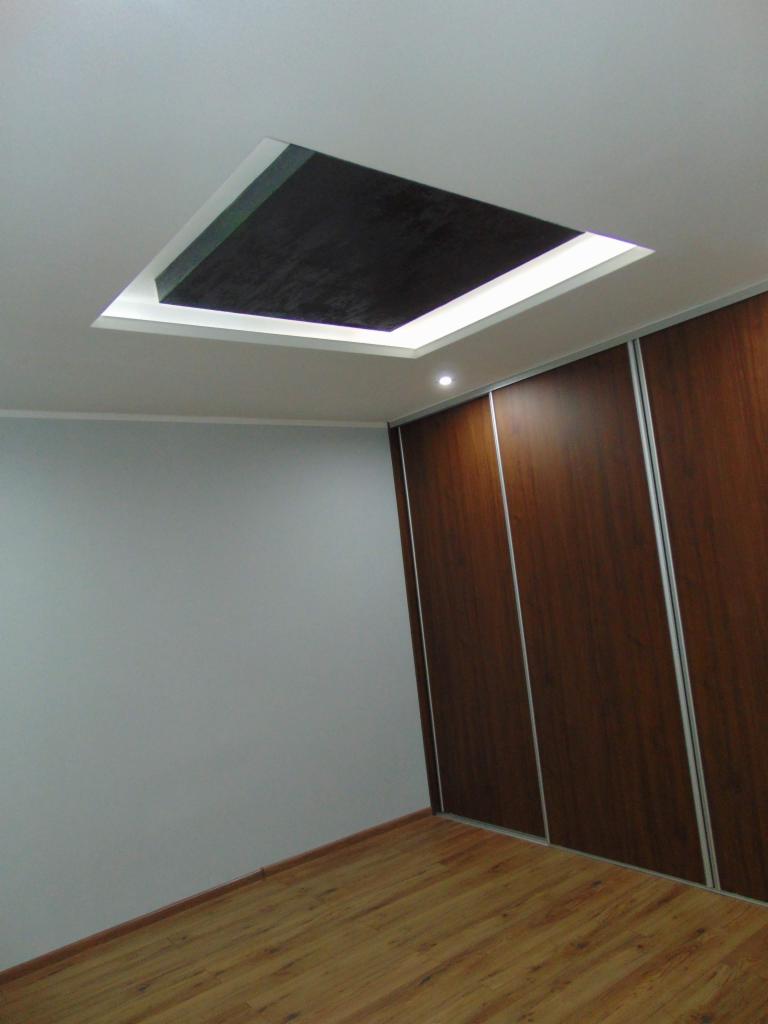 Pokój z drewnianą podłogą i szafą przesuwną, sufit z podwieszanym elementem z oświetleniem LED i ciemną wnęką.