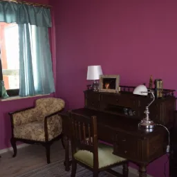 Pokój w odcieniach fioletu z antycznym biurkiem, krzesłem z tapicerką w kwiaty, lampką biurkową w stylu retro i zasłonami w kolorze turkusowym.