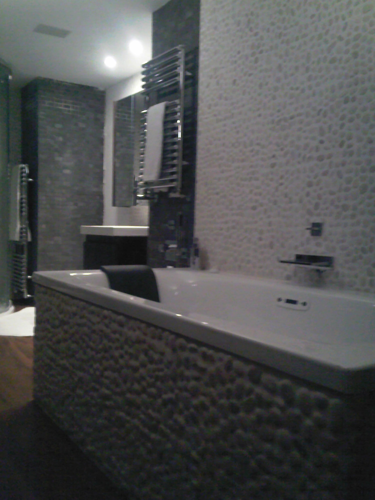 Nowoczesna łazienka z wanną obłożoną mozaiką z kamieni, grzejnikiem drabinkowym i szarą ścianą z płytek.