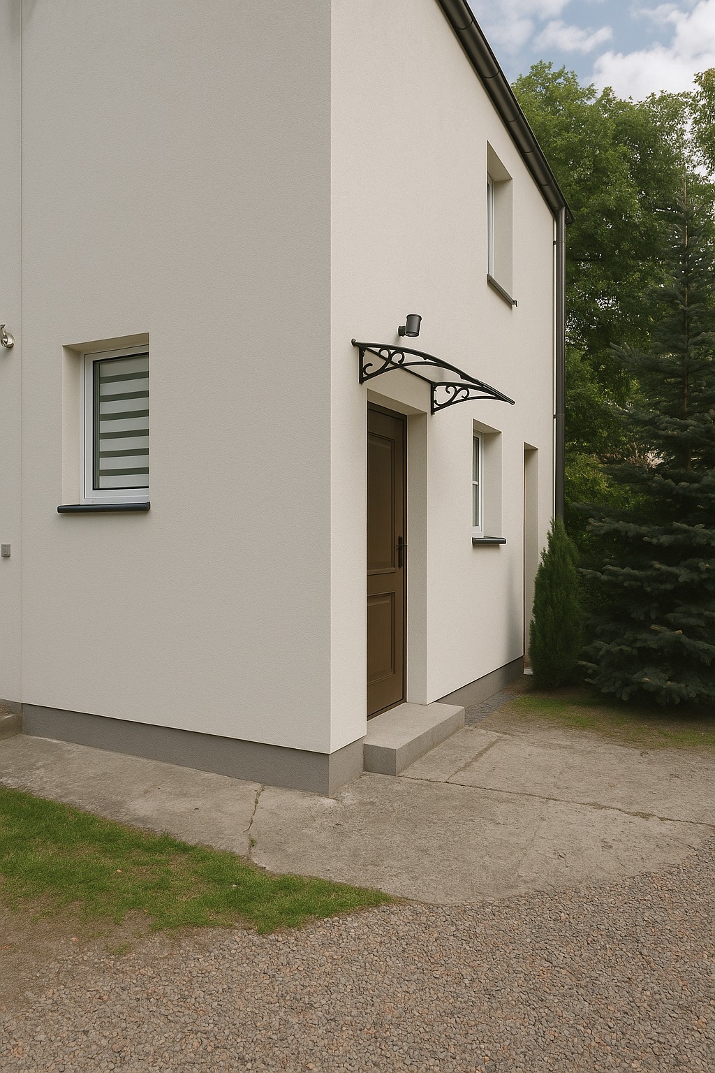 Elewacja domu w jasnym odcieniu z brązowymi drzwiami wejściowymi i ozdobnym zadaszeniem. Widoczne okna z roletami i fragment ogrodu z zielenią.