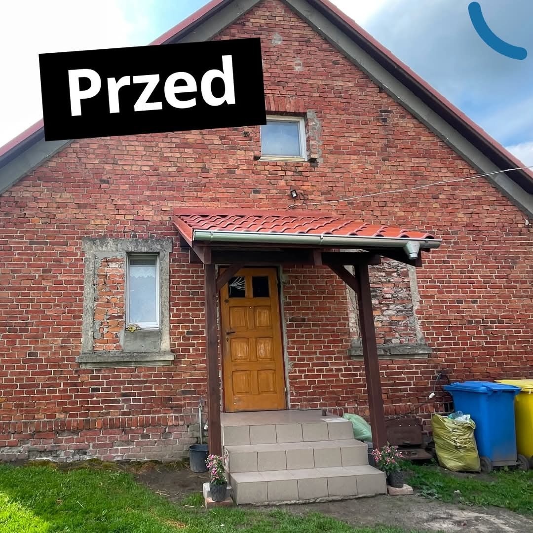 Ceglany dom przed renowacją z oknami i drewnianym gankiem. Widoczne ślady użytkowania i brak ocieplenia. Ujęcie z zewnątrz, w dzień.