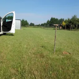 Teren po badaniach geologicznych z widoczną nawierconą próbką gruntu oraz samochodem dostawczym z otwartymi drzwiami w tle.