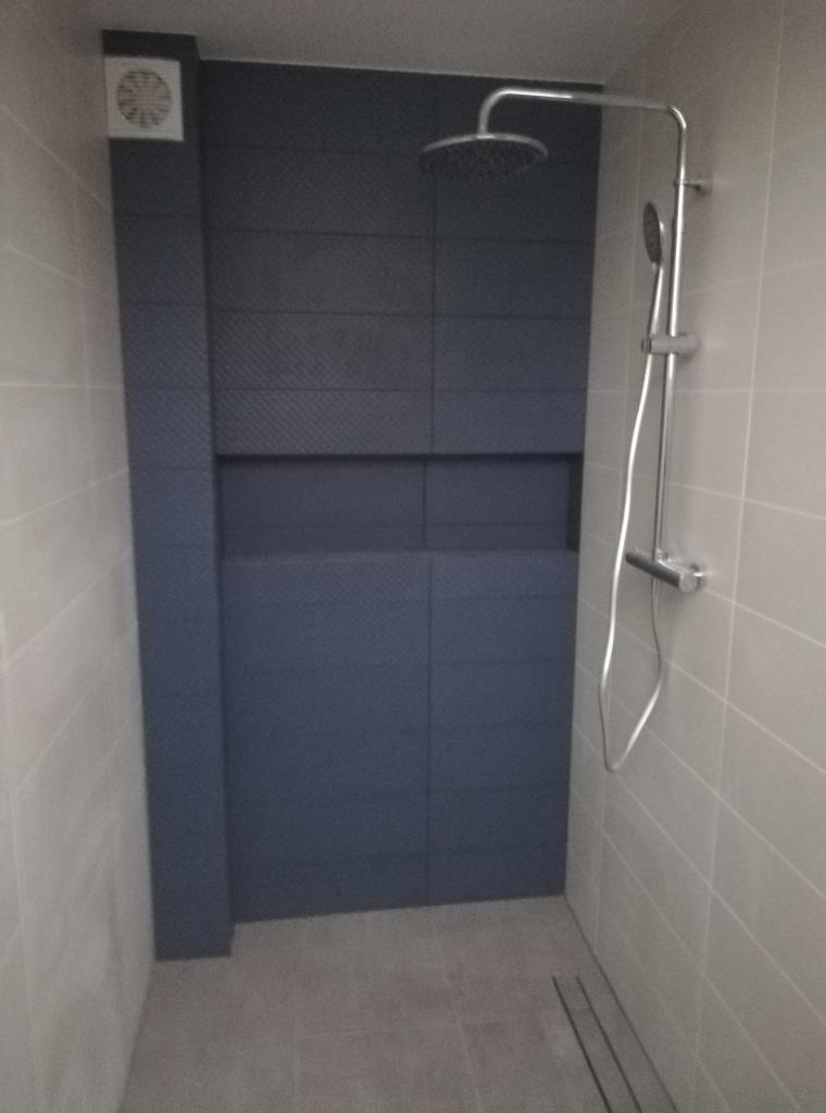 Nowoczesna kabina prysznicowa z ciemnogranatową, teksturowaną ścianą i odpływem liniowym w podłodze.