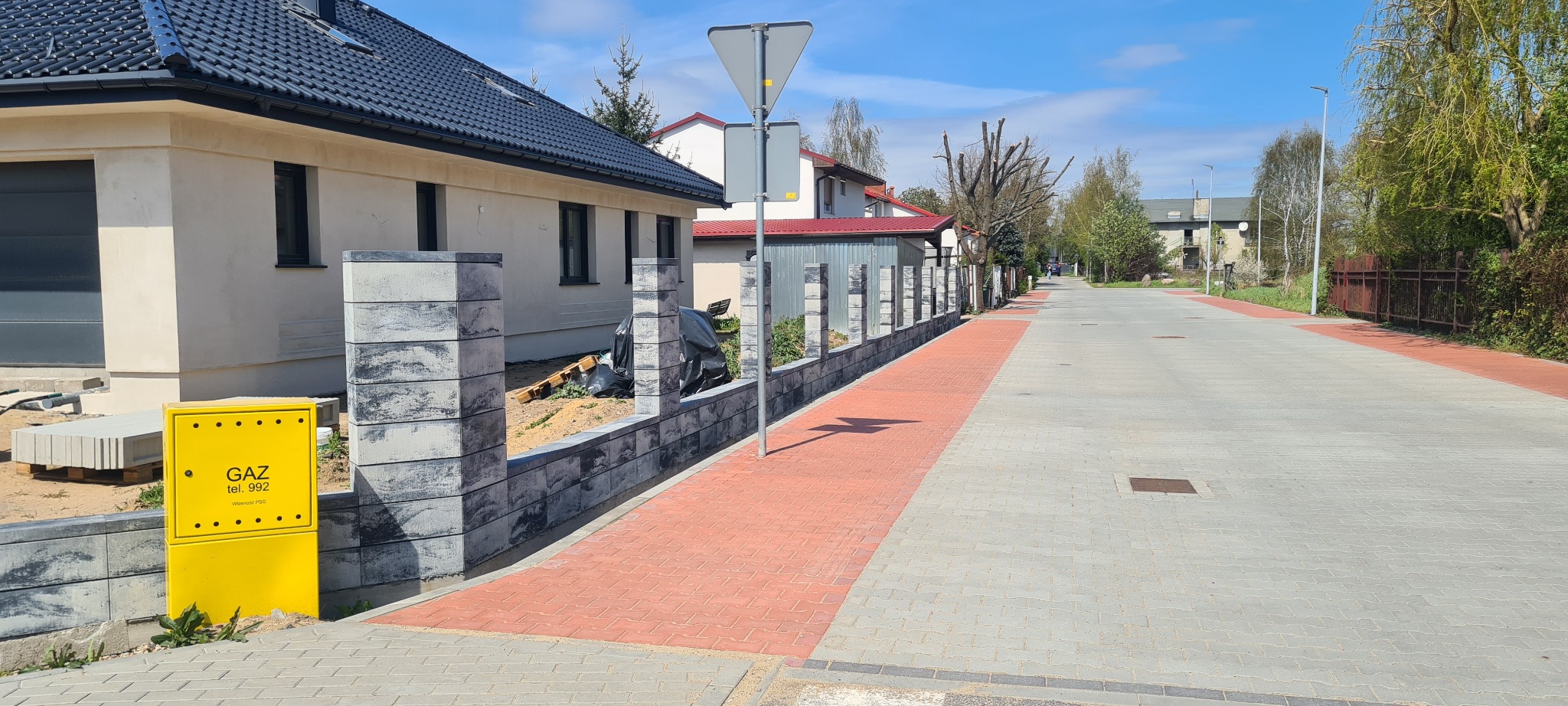 Nowoczesne ogrodzenie modułowe z szarego betonu łupanego, w trakcie montażu, widok z ulicy, żółta skrzynka gazowa w pierwszym planie.