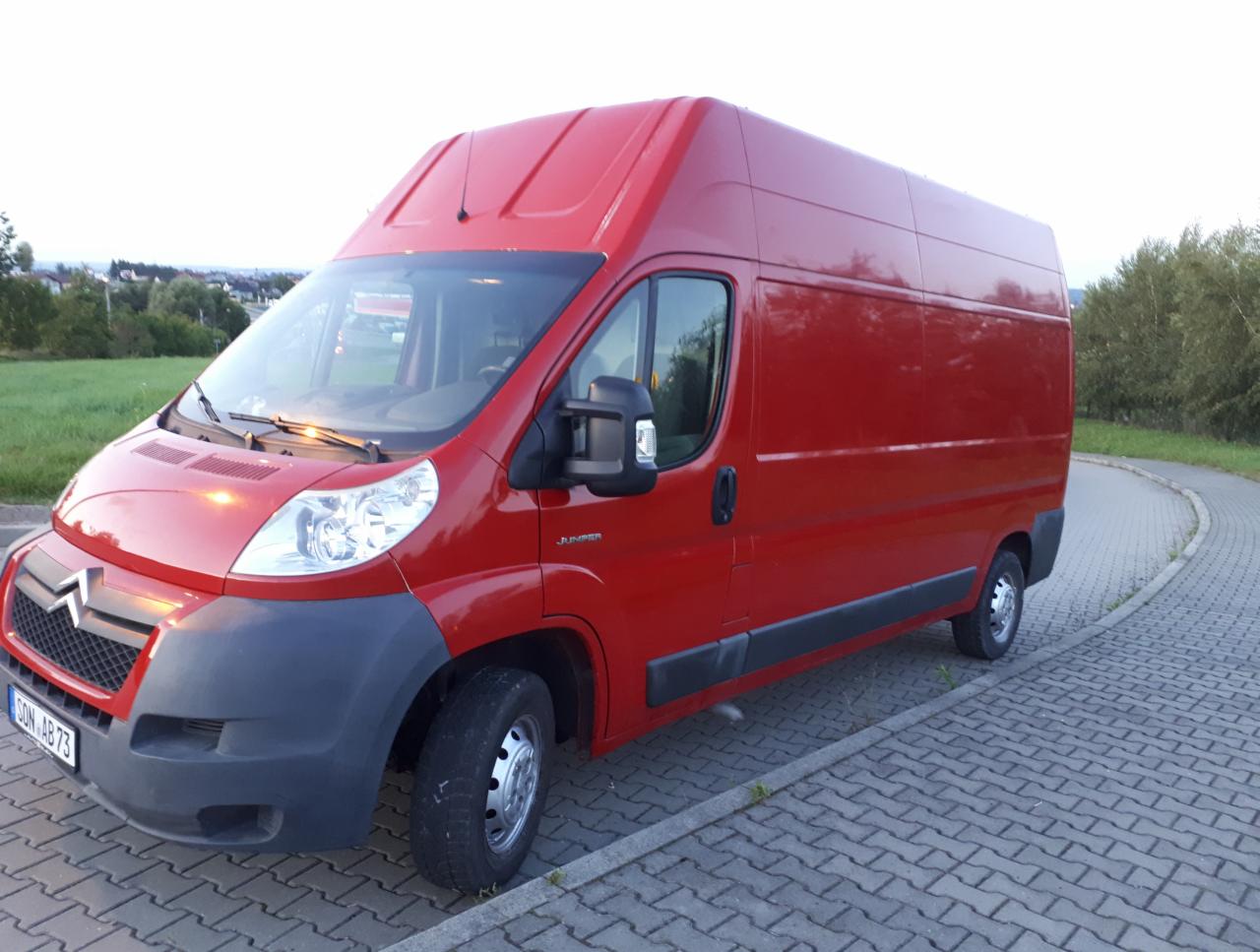 Czerwony Citroen Jumper z wysokim dachem, zaparkowany na kostce brukowej, widoczny z przodu pod kątem.