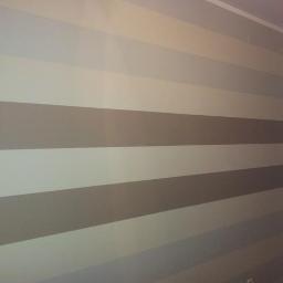 usługi ogulnobudowlane - Ściana pomalowana w poziome pasy w odcieniach szarości i beżu, widoczny fragment sufitu i narożnik pokoju.