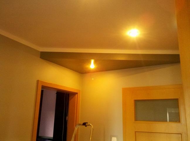 Wnętrze pokoju w trakcie remontu: widoczne pomalowane ściany, sufit z oświetleniem, drzwi wewnętrzne, drabina malarska i listwy wykończeniowe.