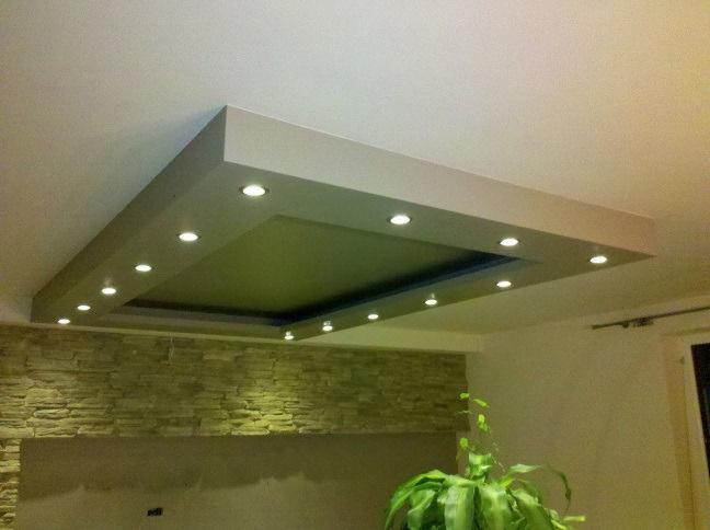 Podwieszany sufit z oświetleniem punktowym w ramie, kamienna ściana w tle i roślina doniczkowa w rogu pokoju.