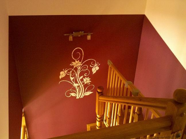 Bordowa ściana z białym, kwiatowym wzorem obok drewnianej balustrady schodów, oświetlona lampą sufitową