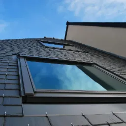 Dach pokryty łupkiem z dwoma oknami dachowymi, w których odbija się błękitne niebo.