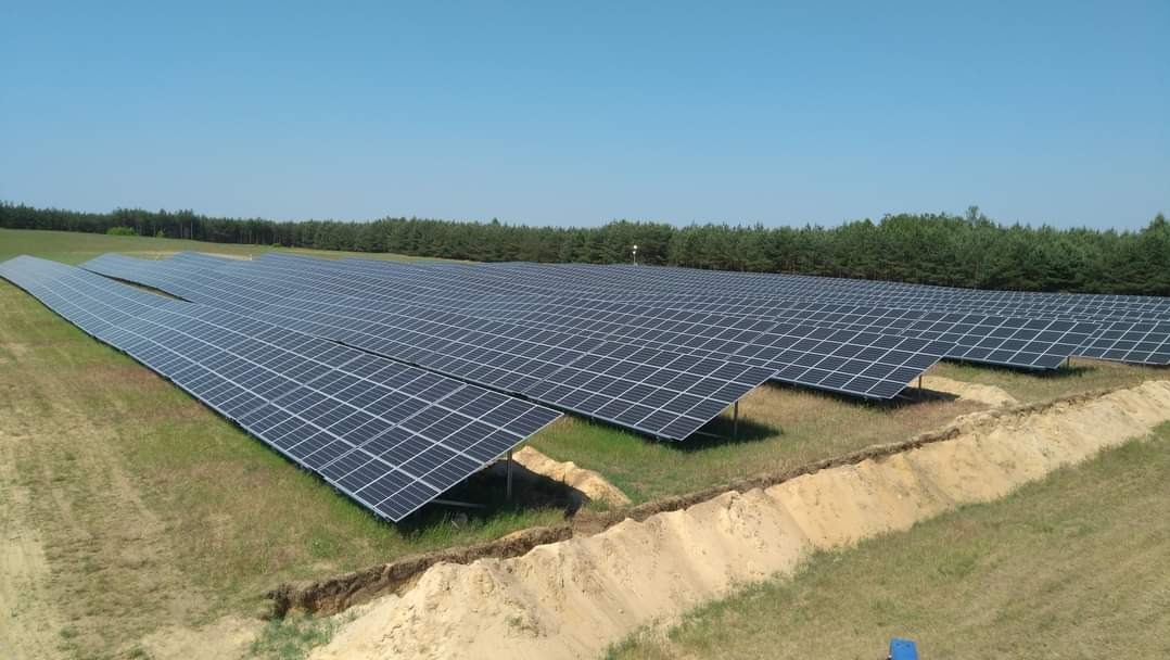 Rozległa farma paneli słonecznych na zielonym polu z wykopanym rowem, widok z góry w słoneczny dzień.
