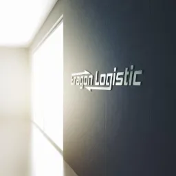 Logo firmy transportowej Aragon Logistic na ciemnoszarej, betonowej ścianie w jasnym korytarzu z oknem.