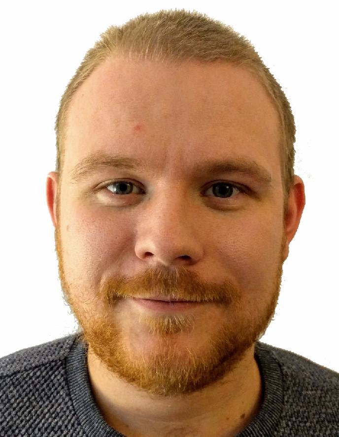 Portret mężczyzny z rudą brodą i krótkimi blond włosami, ubrany w szary sweter o wyraźnej fakturze.