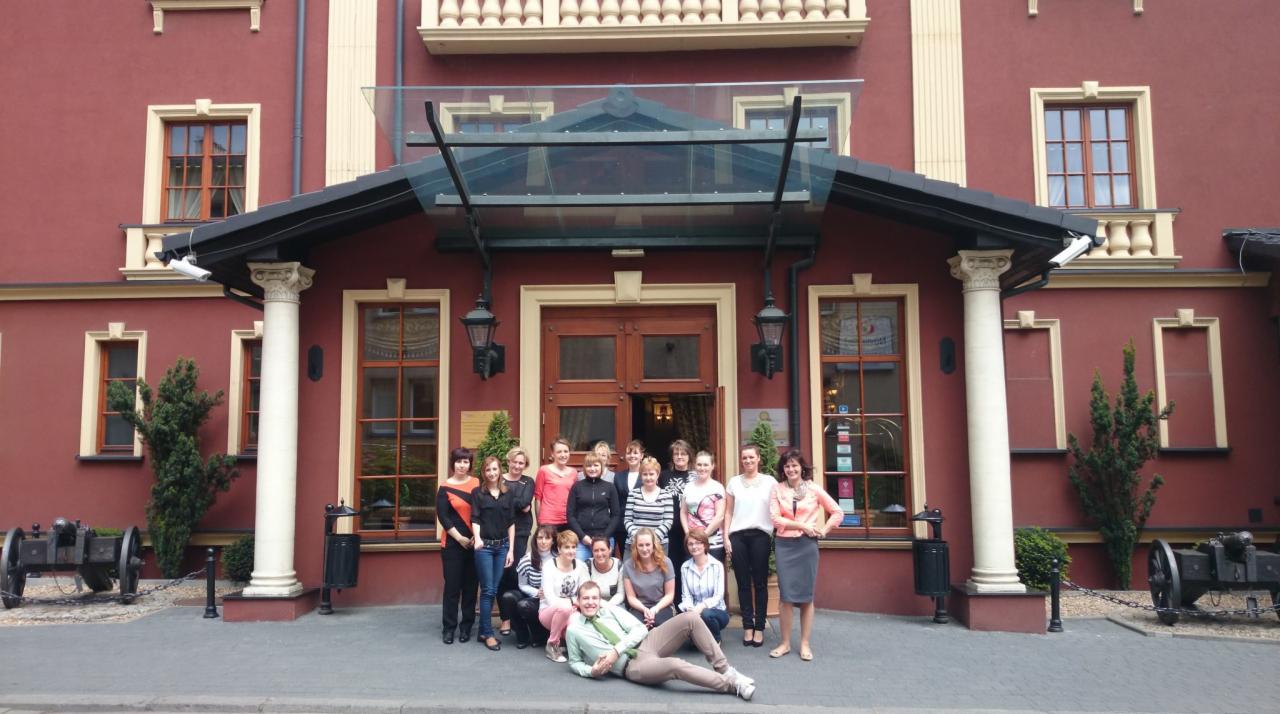 Grupa osób pozuje przed budynkiem z kolumnami i dekoracyjnymi armatami, prawdopodobnie kadra placówki edukacyjnej.