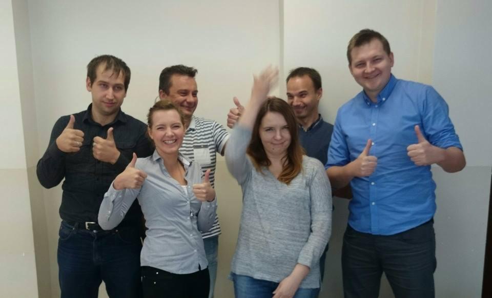 Grupa sześciu uśmiechniętych osób, w różnym wieku, stojących na tle białej ściany i pokazujących kciuki w górę, prawdopodobnie po udanym szkoleniu.