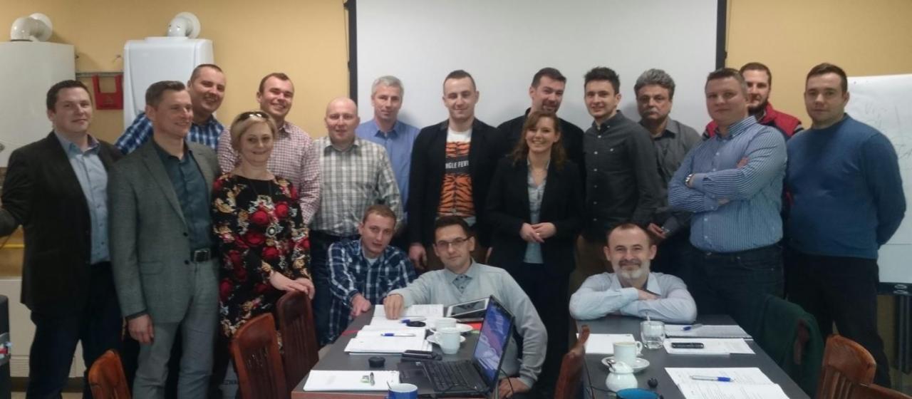 Grupowe zdjęcie zespołu podczas szkolenia lub warsztatów, z widocznymi notatkami i laptopem na stole.